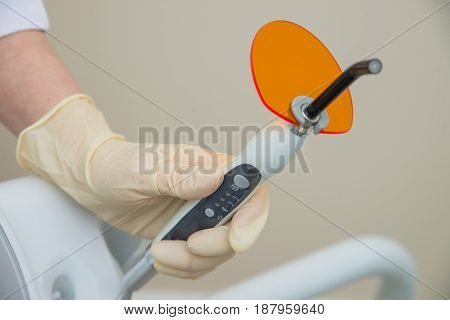 Hand in medical glove holding Dental UV curing light. Ultraviolet polymerization Lamp with orange blocking glass.