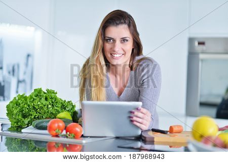 Young woman is making online shopping by tablet computer. Housewife found new recipe for cooking in a kitchen.