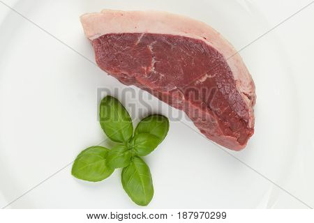 Slice of raw cow beef with some basil leaves isolated in white background - close up