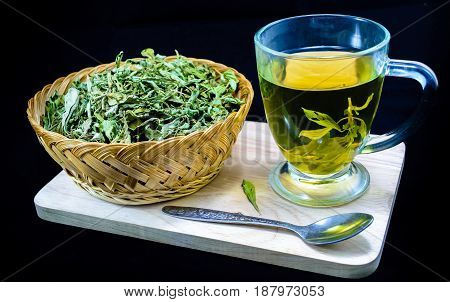 Dry stevia leaves in a small basket and a cup with stevia infusion on black