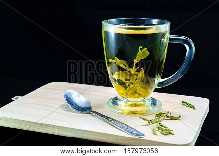 A cup with stevia infusion with spoon steel on wooden bord on black background
