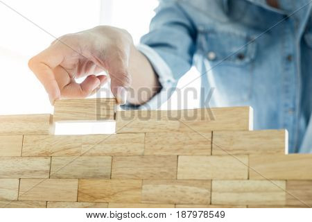 Hand Of Engineer Playing A Blocks Wood Tower Game (jenga) On Blueprint Or Architectural Project Conc