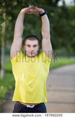 Fitness man stretching arm shoulder before outdoor workout. Sporty male athlete in an urban park warming up