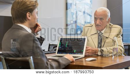 Young financial advisor sitting in front of laptop, consulting senior client with his investment strategy.