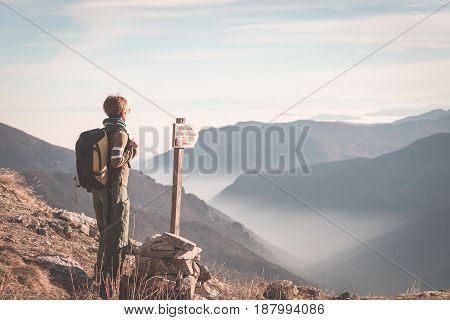 Female hiker with backpack looking at the majestic view on the italian Alps. Mist and fog in the valley below snowcapped mountain peak in the background. Selective focus toned image.