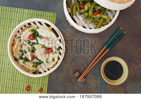 Streamed Gyoza (Jiaozi) and Edamame beans served warm with salt in bamboo steamer. Top view, blank space