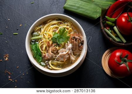 Asian soup noodles and chicken in bowl on dark background. Top view flat lay.