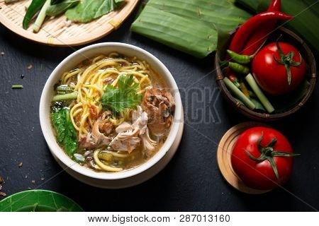 Asian soup noodles and chicken in bowl on dark background. Top view flat lay.