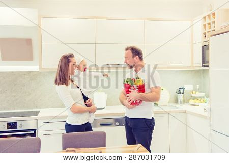 Happy Parents Standing In The Kitchen And Prepares For Cooking With Their Baby Girl Chef. Father Bri