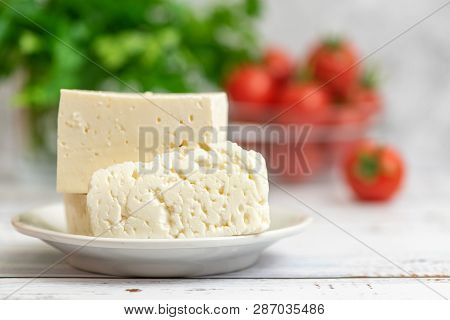 Large Pieces Of Feta Cheese In White Plate And Cherry Tomatoes On Light Background. Selective Focus,