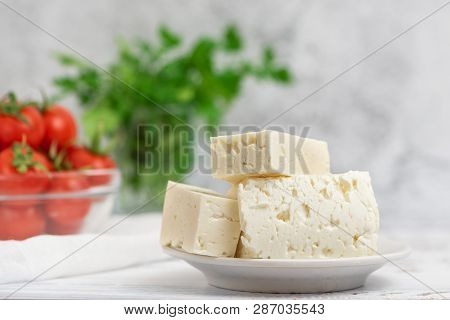 Large Pieces Of Feta Cheese In White Plate And Cherry Tomatoes On Light Background. Selective Focus,