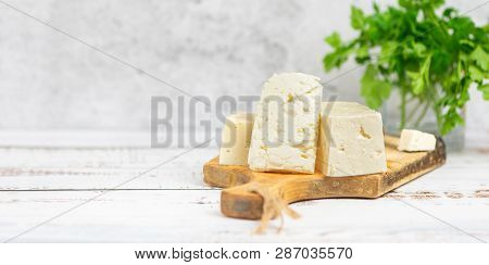Large Pieces Of Feta Cheese On Old Wooden Cutting Board And Parsley On Light Background. Selective F