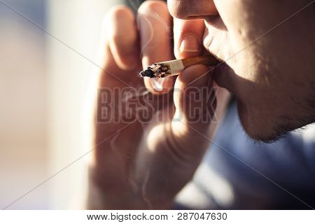 A Young Man, Illuminated By The Sun, With Bristles On His Chin Makes The Last Puff Of A Cigarette Bu