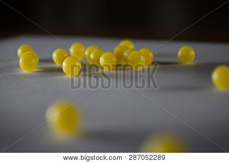 Dark Soft Focus Close Up Of Multiple Small Yellow Balls Candy Bbs Or Pills On A Gray Paper With Blac