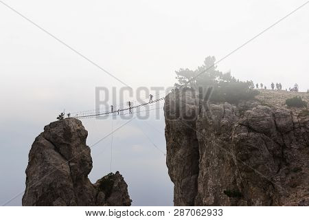 Skybridge, Rope Bridge On The Trident Ai-petri On A Foggy Morning. Silhouettes Of Tourists Walking O