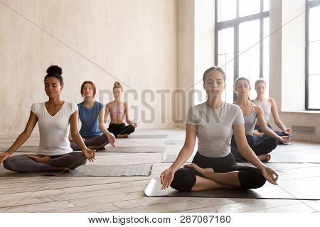 Group Of Young Women Practicing Yoga, Ardha Padmasana Exercise