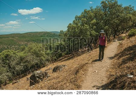 Monfrague Park, Spain - July 04, 2018. Woman Walking Through Dirt Path Amid Forest Glade In A Sunny 