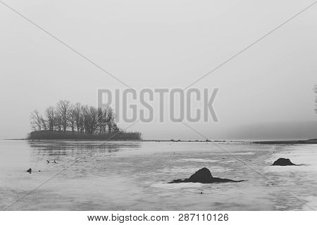 Black And White Photo Of Island In The Middle Of Lake Covered With Meting Ice At Beginning Of Spring