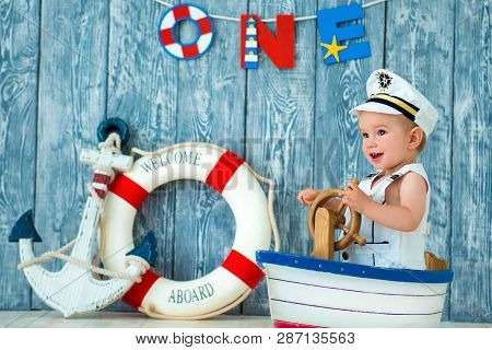 Photoshoot For A Boy Of One Year. Little Sea Captain, Sailor On Toy Ship With Steering Wheel. Sea An
