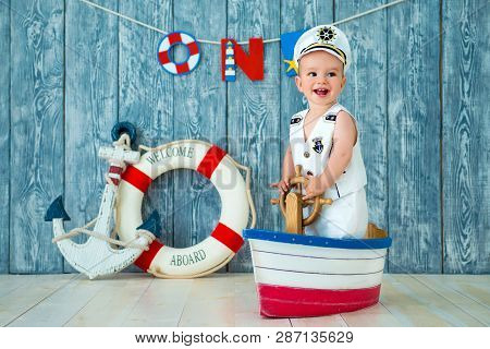 Photoshoot For A Boy Of One Year. Little Sea Captain, Sailor On Toy Ship With Steering Wheel. Sea An