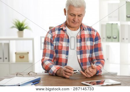 Senior Man Using Digital Glucometer At Table. Diabetes Control