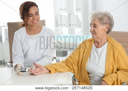 Doctor Checking Patient's Blood Sugar Level With Digital Glucometer At Table. Diabetes Control