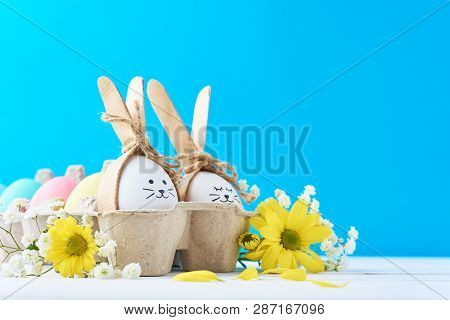 Easter Colored Eggs In Paper Tray With Decorationd On Blue Background