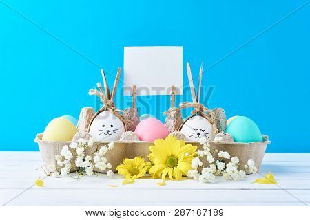 Easter Colored Eggs In Paper Tray With Decorationd On Blue Background