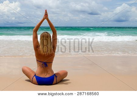 Young Woman Makes Meditation In Lotus Pose Oon Tropical Beach With Waves Harmony And Contemplation.