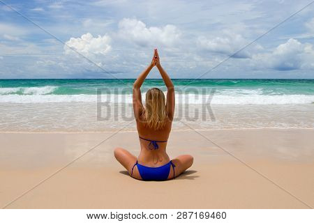 Young Woman Makes Meditation In Lotus Pose Oon Tropical Beach With Waves Harmony And Contemplation.
