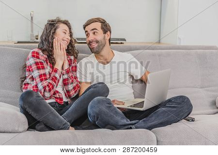 Smiling Young Couple Enjoying Time Spent At The Computer, Sitting On The Couch At Home Together, Hap