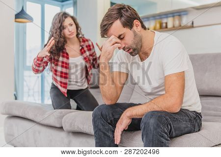 Couple Argue. The Wife Shouted To Her Desperate Husband, Sitting On The Couch In The Living Room At 