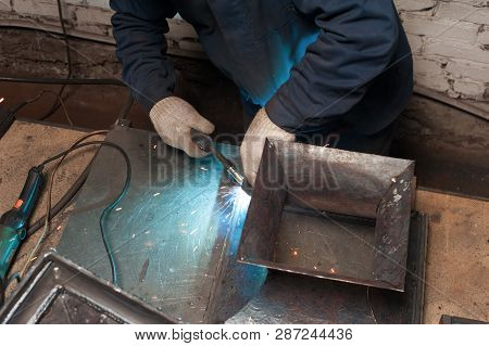 Blacksmith Soldering Metal Plates To A Metal Stand With Ornament. The Blacksmith In White Blacksmith