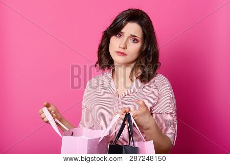 Disappointed Dark Haired Woman, Wears Rose Blouse, Holds Opened Bag. Beautiful Brunette Looks Unhapp