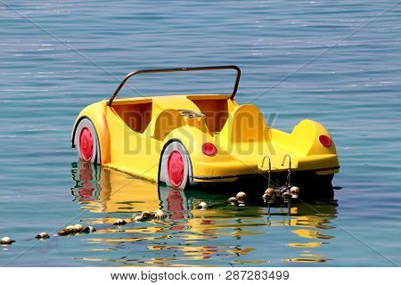 Plastic Yellow Paddle Boat In Shape Of Car Floating On Calm Sea Tied To Shore With Strong Rope And M