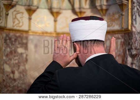 Emam in mosque with verses from Kuran on the wall