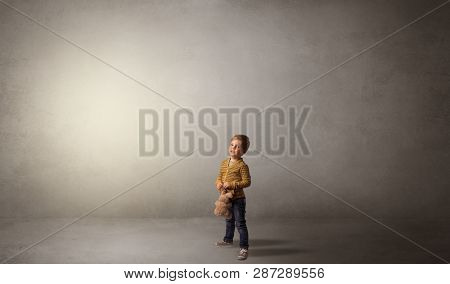 Little waggish kid staying alone in a big empty room with his plush