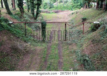 Severed Rusted Metal Pipes With Broken Insulation On Overgrown Support Connecting Two Sides Of Canal
