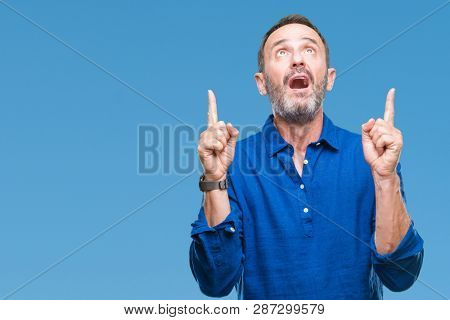 Middle age hoary senior man over isolated background amazed and surprised looking up and pointing with fingers and raised arms.