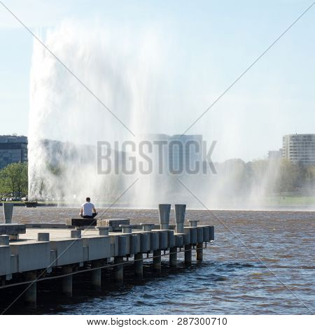 Man Sitting On Jetty Looking At Water Fountain
