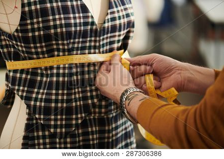 Contemporary tailor measuring girth of dummy chest while working over new dress or suit in studio