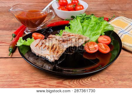 Grilled Steaks Of Pork Neck On Lettuce Leaves And Cherry Tomatoes On Black Dish, Souce, Greens And V