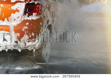Car Is Cleaning With Soap Suds At Self-service Car Wash. White Lather On Auto. Water Splashes Around