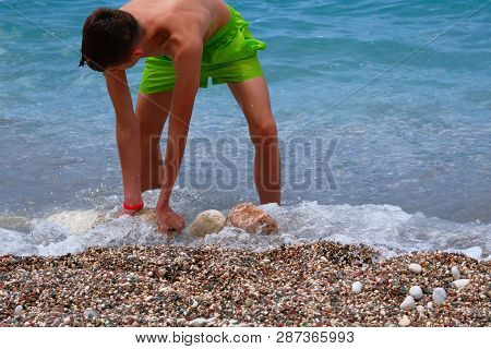 Children Summer Vacation At Sea. Sunburnt School Boy Builds A Tower Of Stones On Sea Coast. Active S