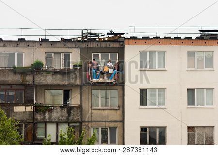 Two Workers Are Plastering The Facade Of A Building Without Observing Safety Techniques In A Cradle 