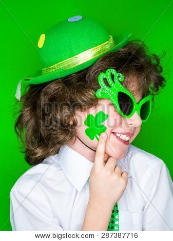 Child Celebrating St. Patricks Day Showing His Make-up. A Small Curly Boy In Green Carnival Accessor