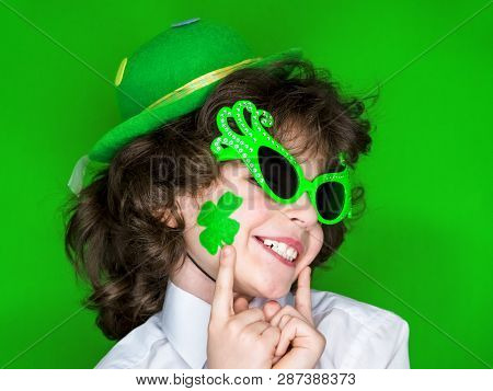 Child Celebrating St. Patricks Day Showing His Make-up. A Small Curly Boy In Green Carnival Accessor