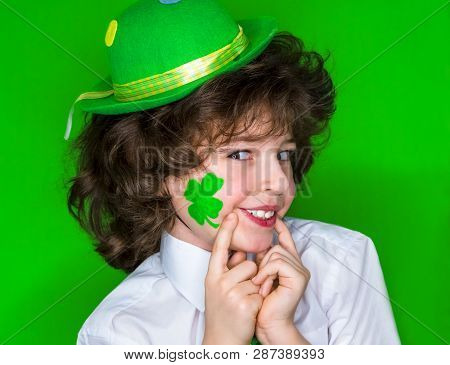 Child Celebrating St. Patricks Day Showing His Make-up. A Small Curly Boy In Green Carnival Accessor