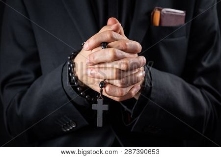 Christian Person Praying, Low Key Image. Hands Of A Man In Black Suit Or A Priest Portraying A Preac