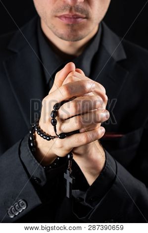 Christian Person Praying, Low Key Image. Hands Of A Man In Black Suit Or A Priest Portraying A Preac